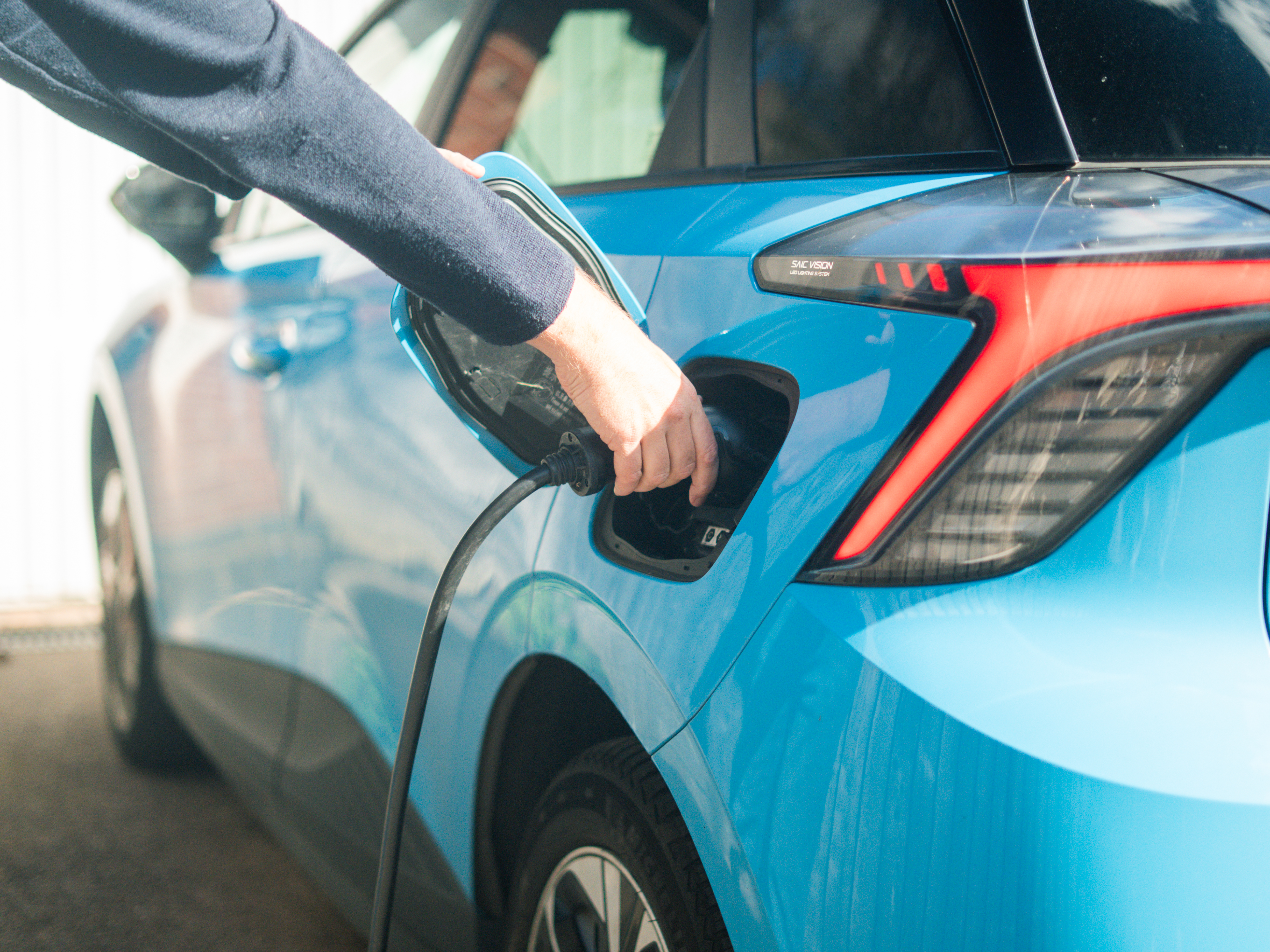 a hand plugging an EV charger to a blue electric vehicle