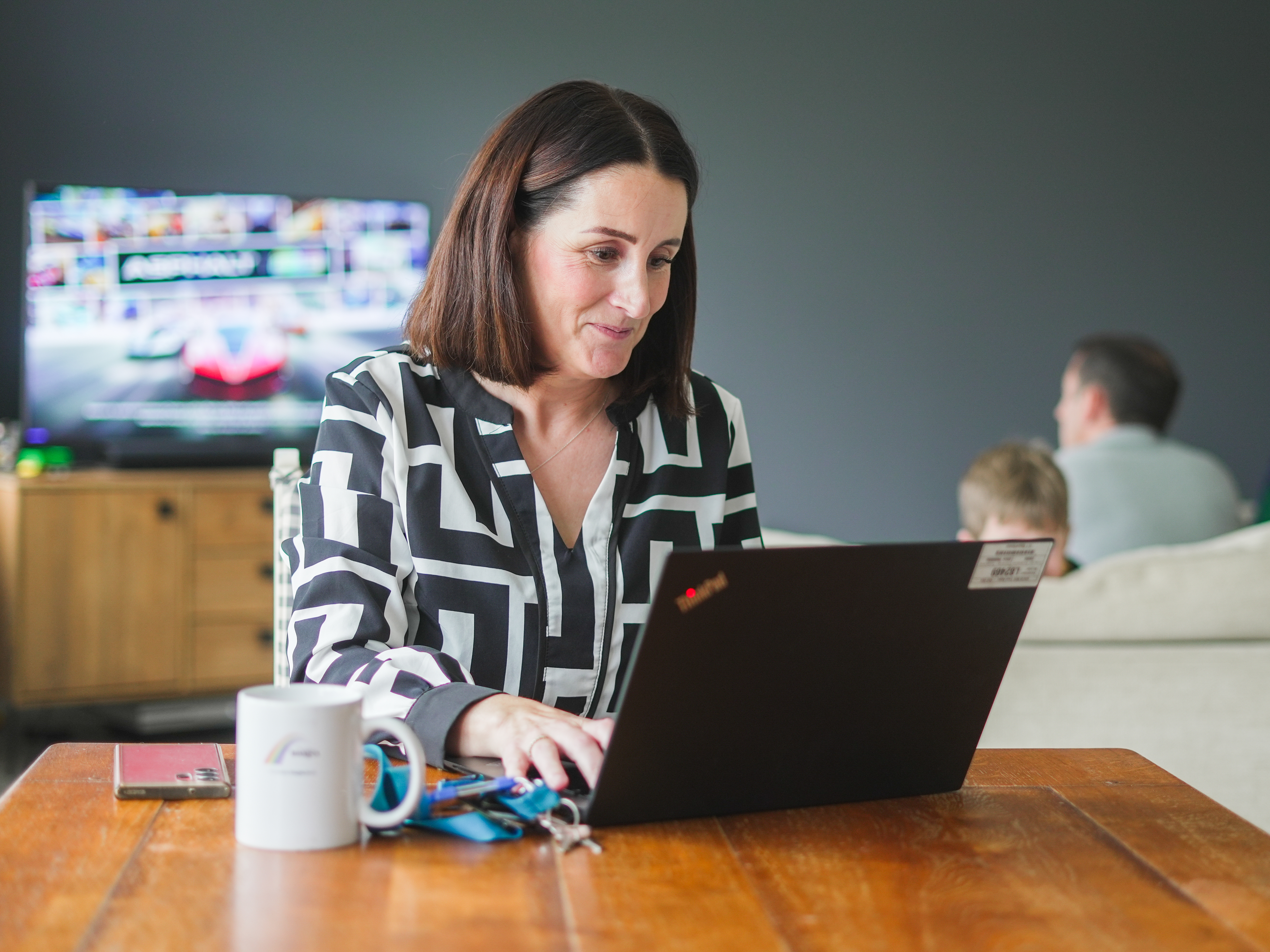 a woman seated at the table looking at her laptop and smiling