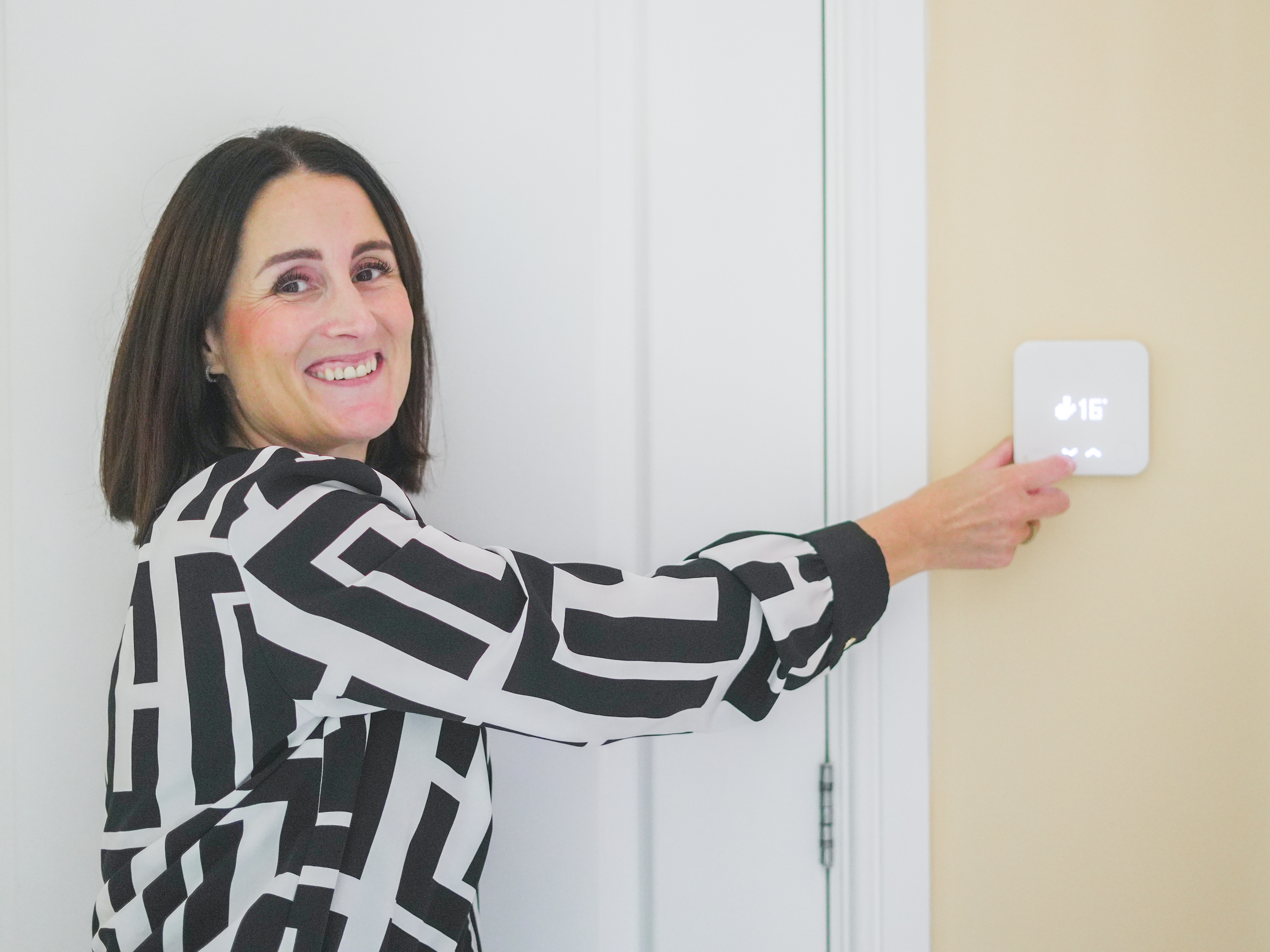 a woman smiles and touches a tado device on the walll